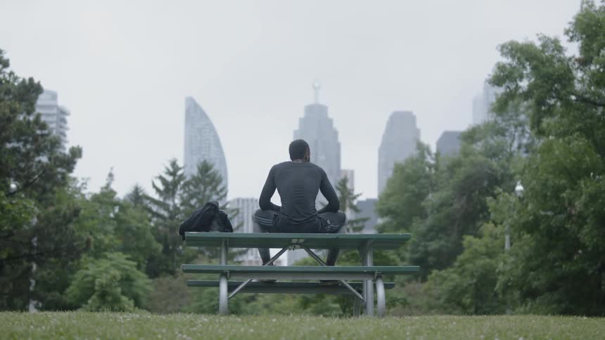 Man sits on top of a picnic table in the park