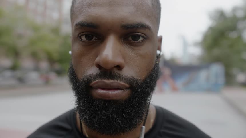 A black man wearing ear buds stands on a basketball court