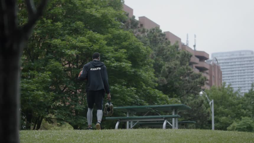 Man in sportswear walks through a park carrying a basketball