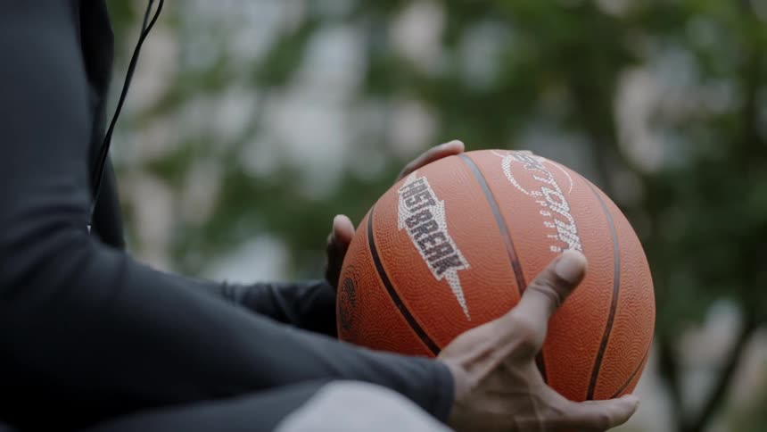 Black man sitting listening to music and holding a basketball