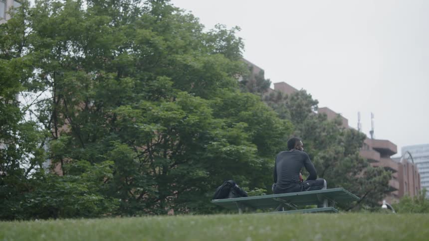 A young black man sits on top of a picnic table