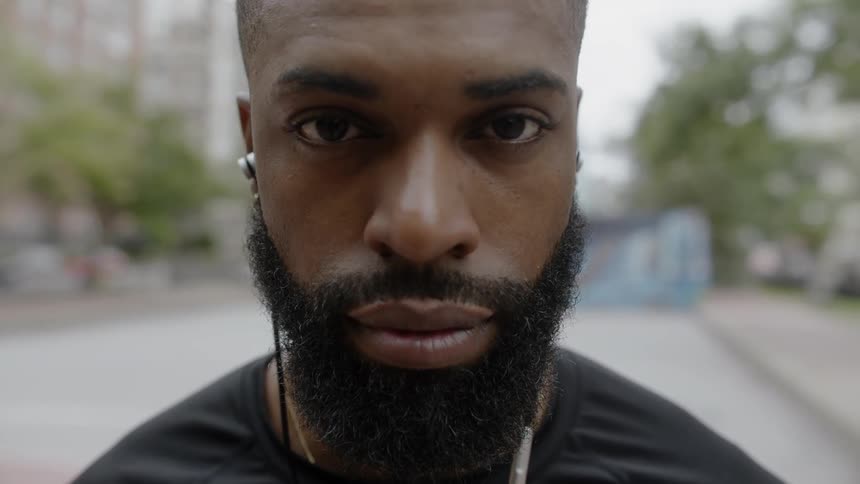 A black man stands and wears headphones as he looks forward