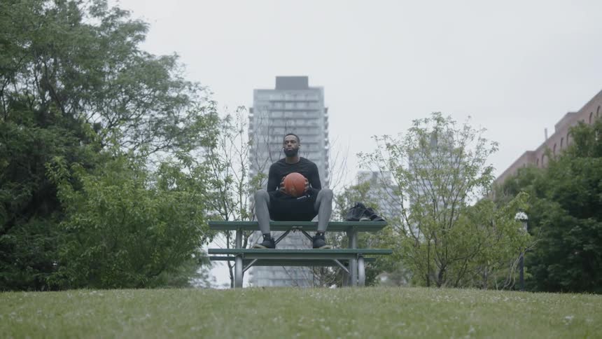 A man sitting on a park bench playing with a basketball
