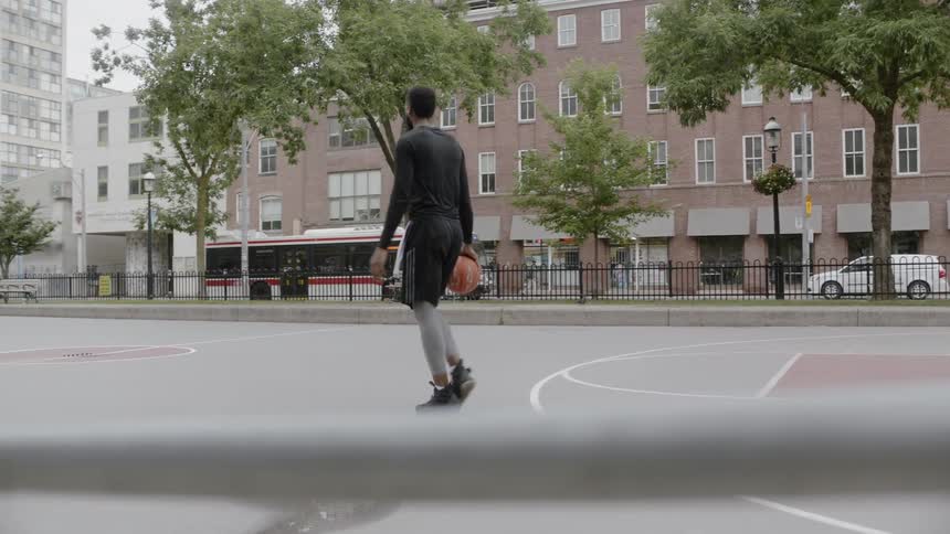 A young black man walks along the sidewalk carrying a basketball