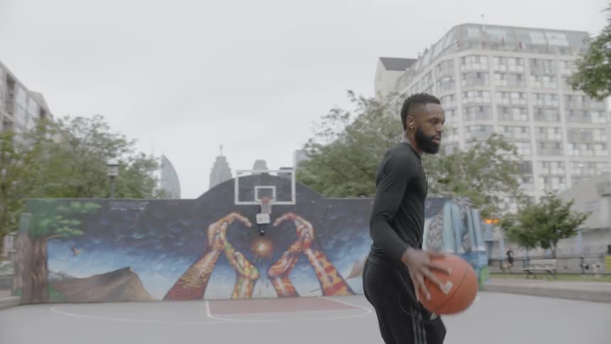 Black man training basketball on a public court in the middle of the city