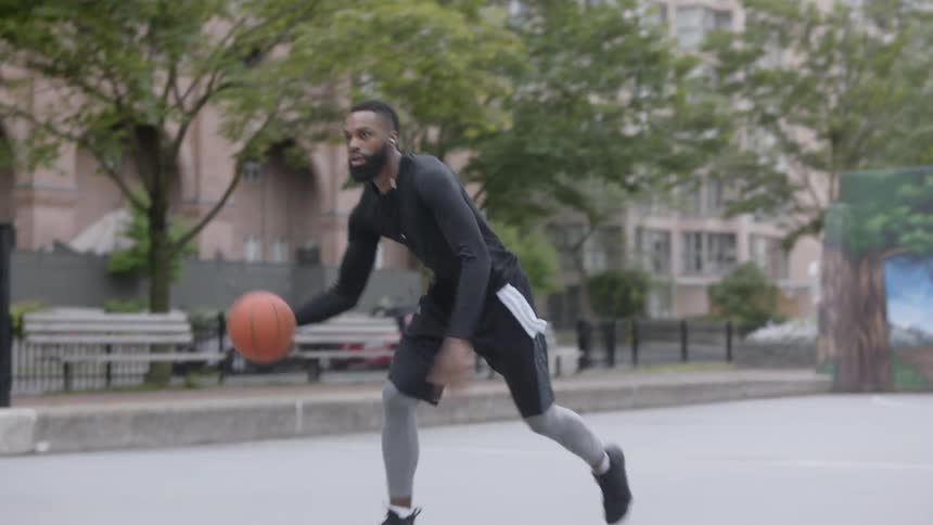 A young black man plays basketball on a court in a city