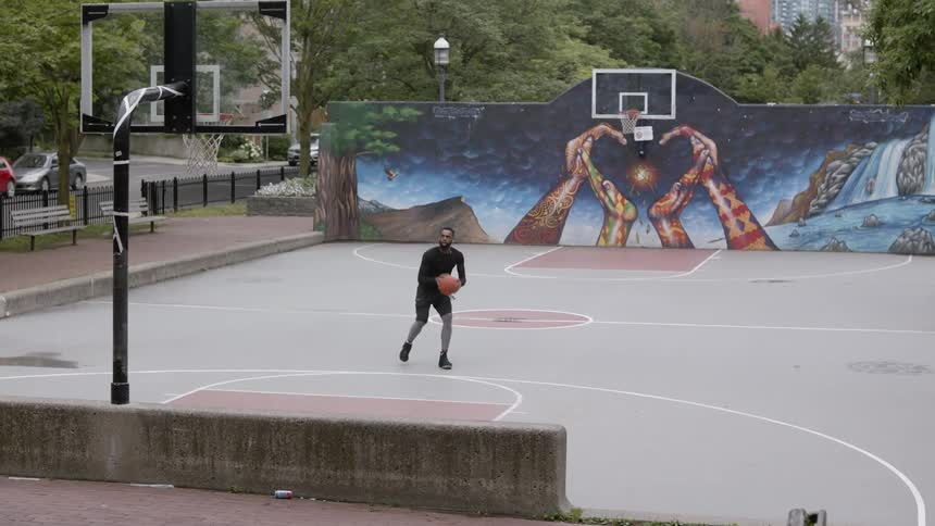 Black man training basketball on a public court in the middle of a city