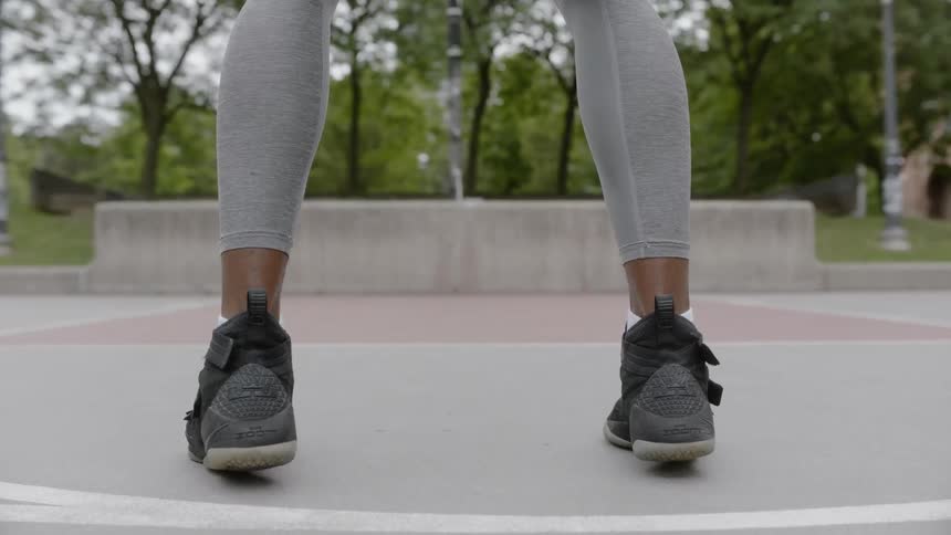 A muscular young black man is wearing high top basketball shoes and sports apparel as he begins to dribble the ball before making a sudden break to a nearby outdoor basketball hood and lays in the ball