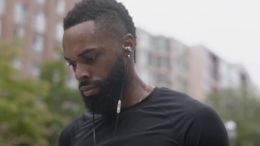 Bearded black man wearing earphones looks down and breathes in the city on a cloudy day