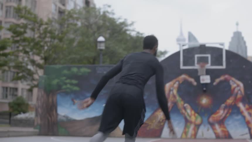Man dribbles a basketball on a court then goes for a layup