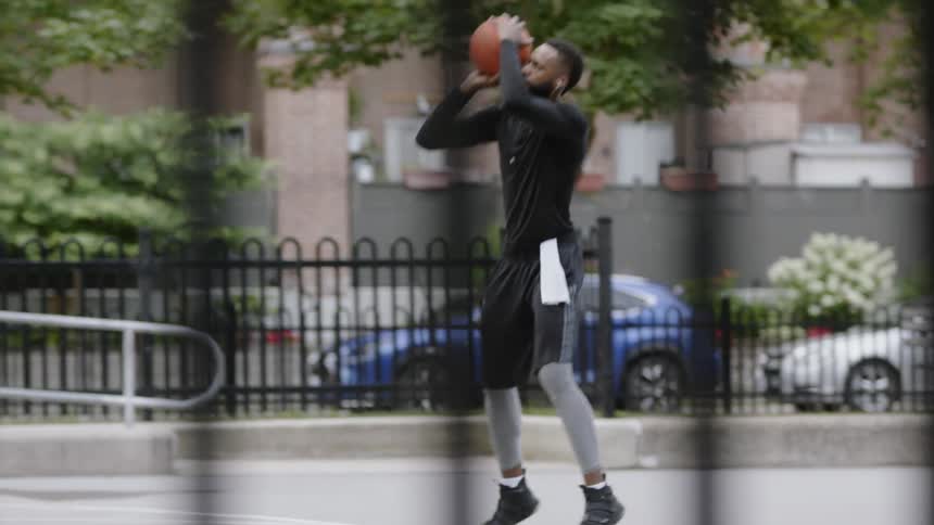 Black man wearing earphones makes a basket in the basketball field in the daytime