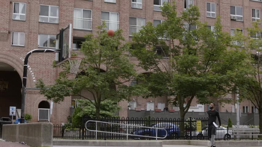 A man takes a jump shot at an outdoor hoop and hits the rim
