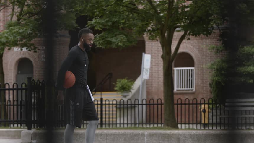 Black man holding a basketball at a basketball court near a building