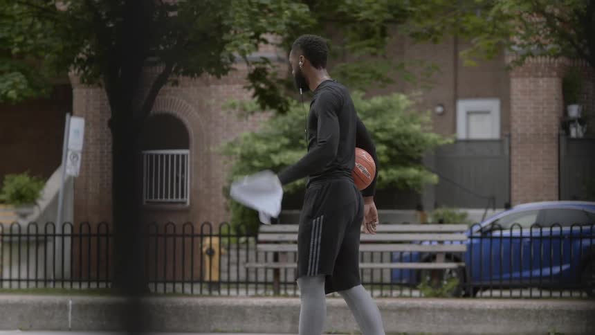 A man in sportswear walks on a basketball court carrying a ball