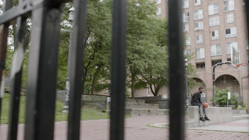 Man sits on wall under basketball hoop outdoors in park