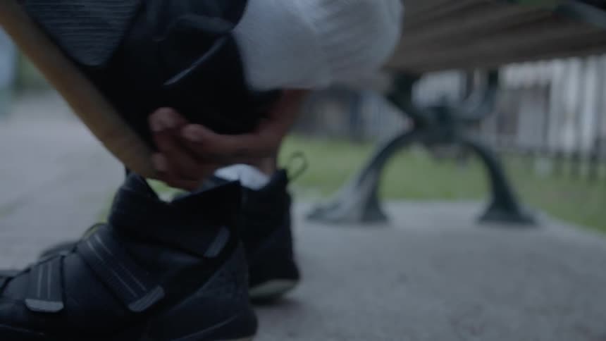 A black person sitting on an outdoor bench and removing their shoe