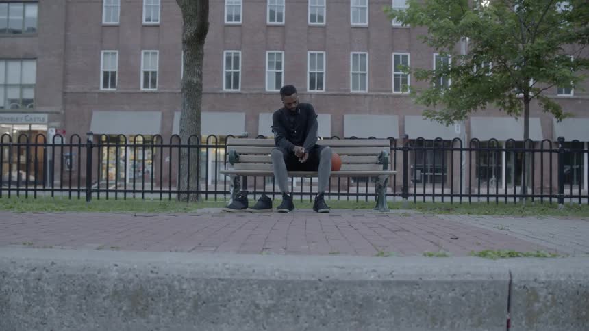 Black man sitting on the bench next to a basketball