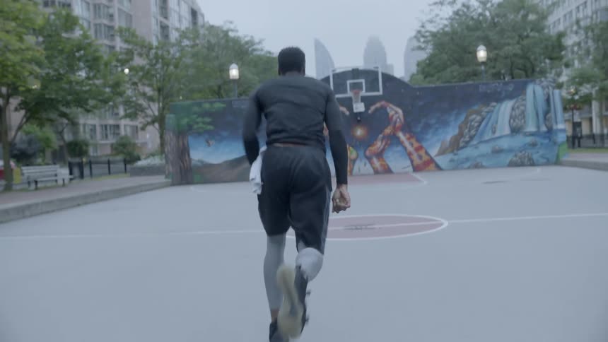 A black man runs back and forth on an urban basketball court