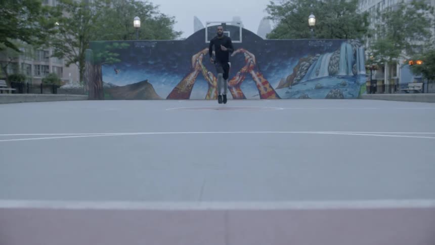 A black man runs up and down an urban basketball court
