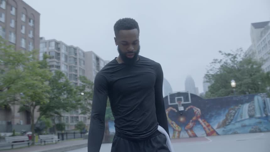 Young black man walks across outdoor basketball court with mural
