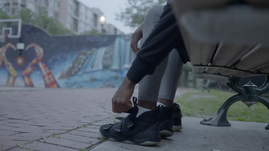 A young black man with a basketball is changing his shoes