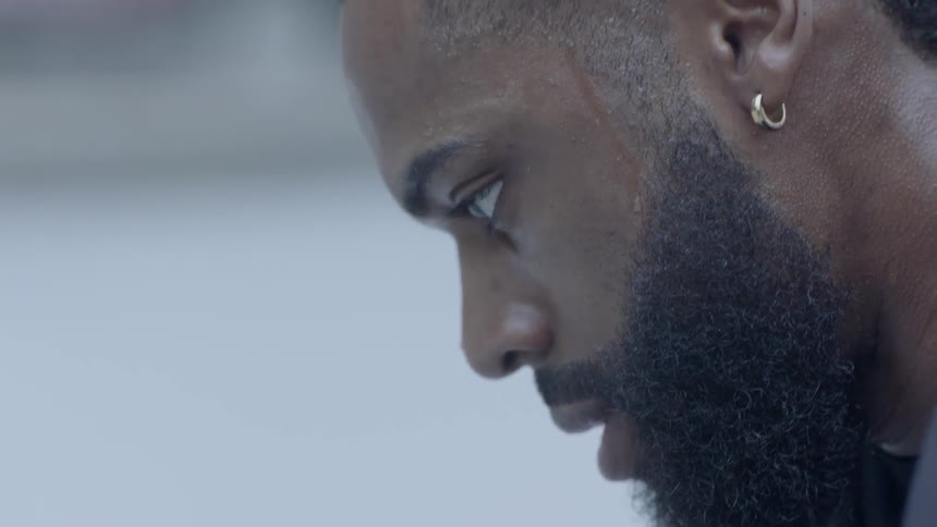 Bearded black man wearing earrings looks down and thinks in the daytime
