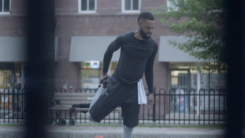 A man holds his foot to stretch his thigh in a park
