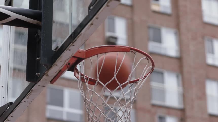 A basketball flies through a basketball hoop on an outdoor court