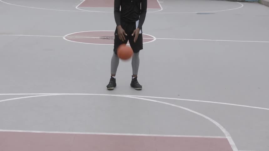 A black man dribbles a basketball on a basketball court