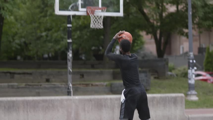 A man in a outdoor court dribbling and shooting a basketball