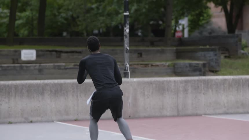 Bearded black man who wears earphones shoots a basket in the basketball field by day