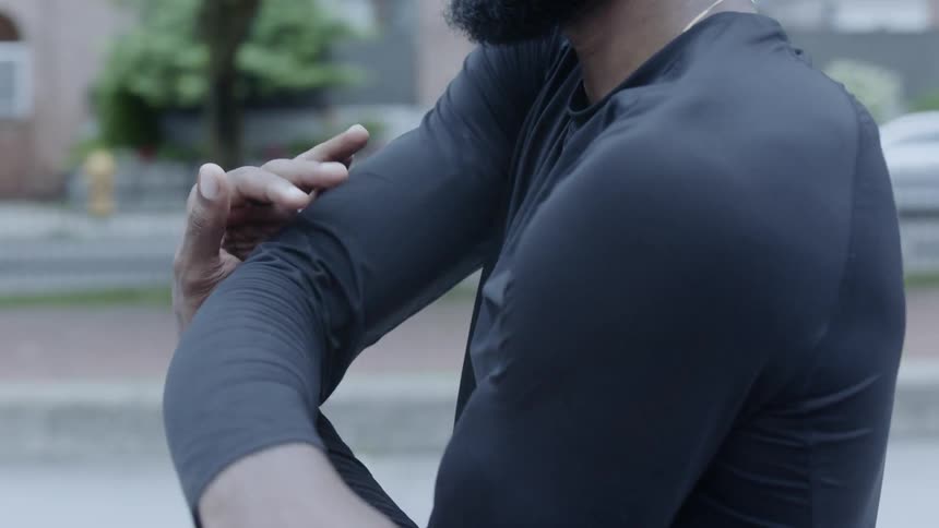 A man standing in a city park stretching his arms