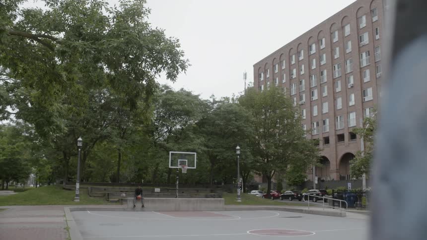 Man holding basketball sits down on concrete wall in basketball field on a cloudy day