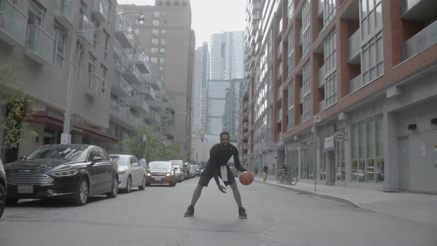 A black man dribbles a basketball in the middle of a city street