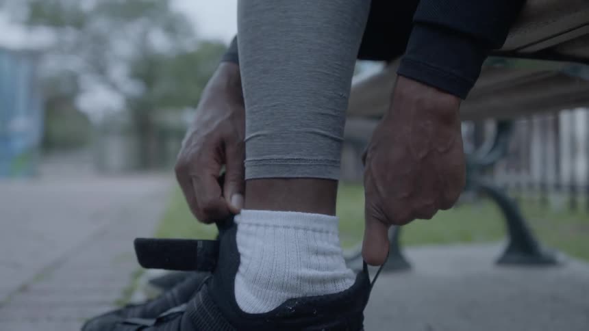 Man puts on sneakers while sitting on a bench