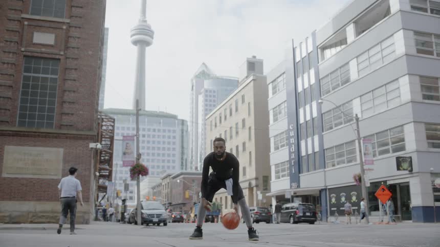 A man dribbles a basketball on a city street with people walking past