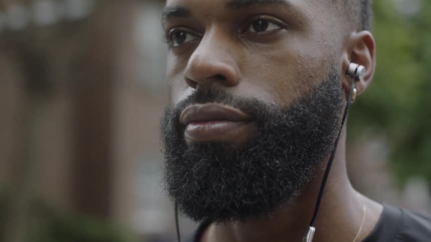Man wearing earphones stands outdoors staring