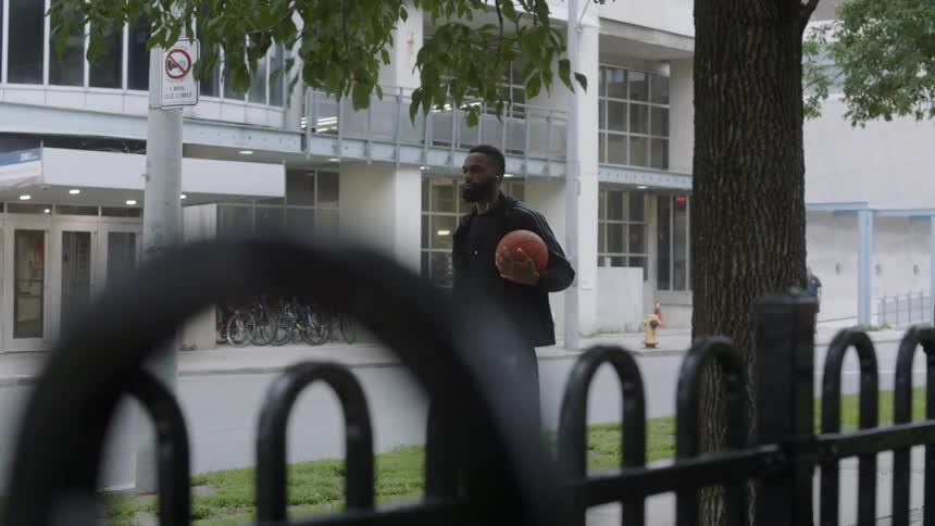 Man walks down a sidewalk carrying a basketball and shoes