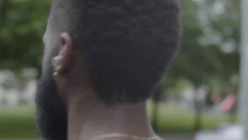 A black man with ear buds walks down a city sidewalk