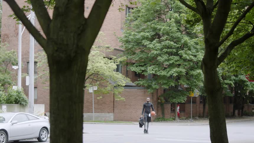 Young black man with a basketball ball in his hand crosses the street