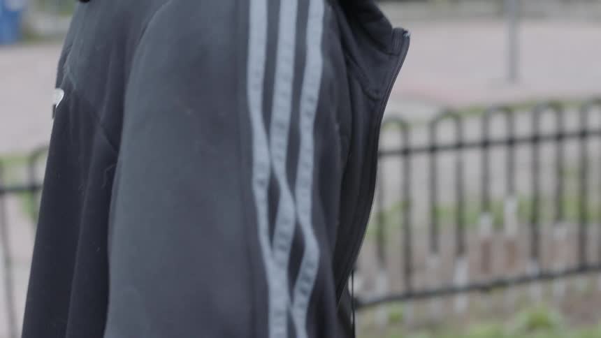 Bearded black man wearing earphones walk on the pavement and carries basketball on a cloudy day