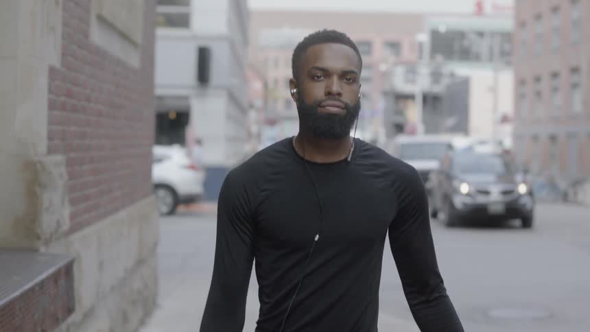 Black man walking down a sidewalk while holding a basketball and wearing a earphone