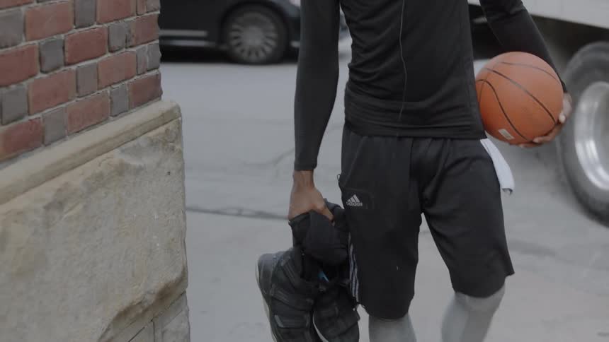 A man walking on the sidewalk holding a basketball and sneakers