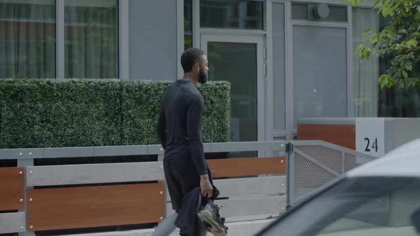 A man walks along a city sidewalk carrying a basketball and sneakers