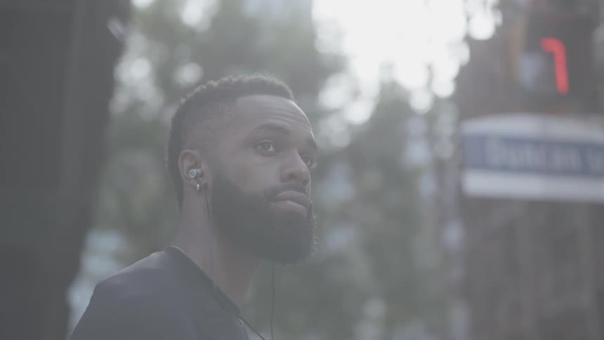 A black man wearing ear buds looks around the city