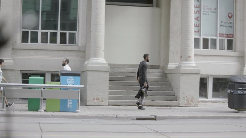 A young black man walks down a sidewalk with a basketball