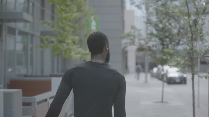 A black man wearing ear buds walks down a city sidewalk