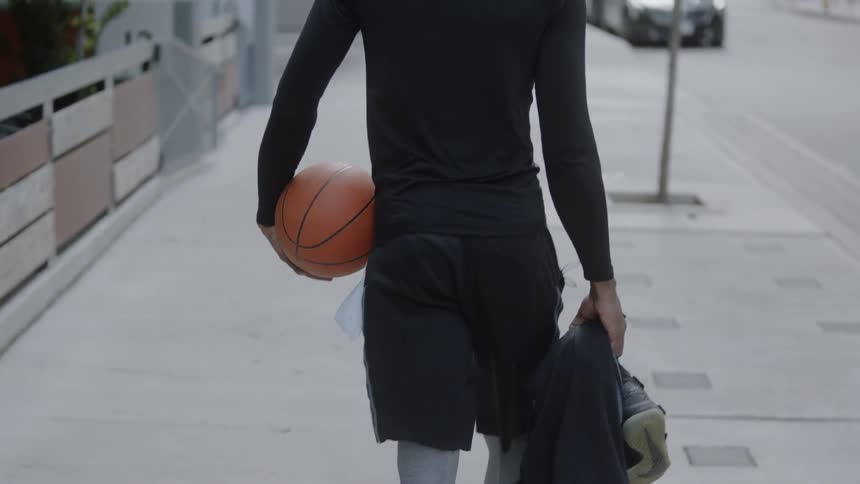 Man holding clothes and basketball walks down the street in the daytime