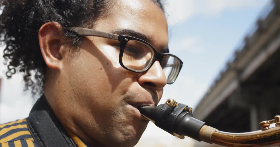 Young man plays saxophone near overpass