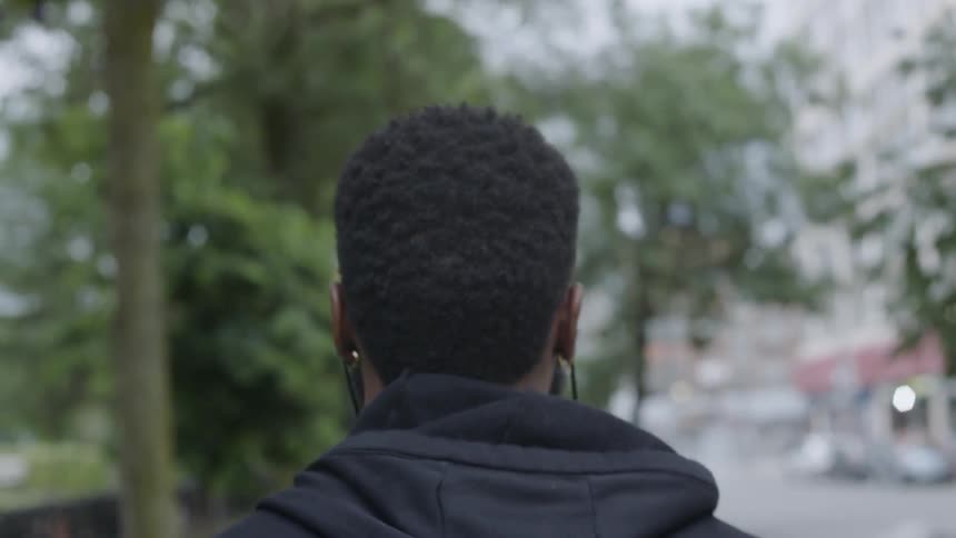A black man wearing ear buds saunters down a city sidewalk